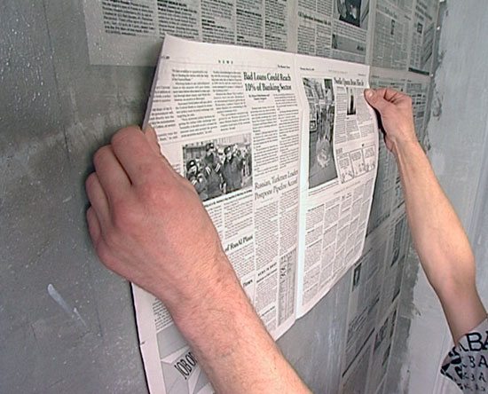 На фото – наклеивание газеты на стену