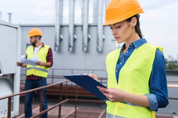 Female Architect Helmet Writing Clipboard Roof Male Colleague Blueprint — стоковое фото